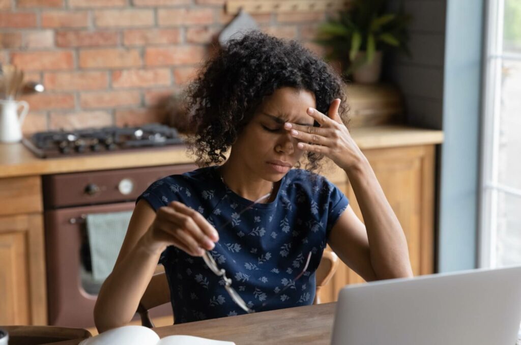 Woman rubbing her forehead and eyes, experiencing dry eye and headache symptoms.