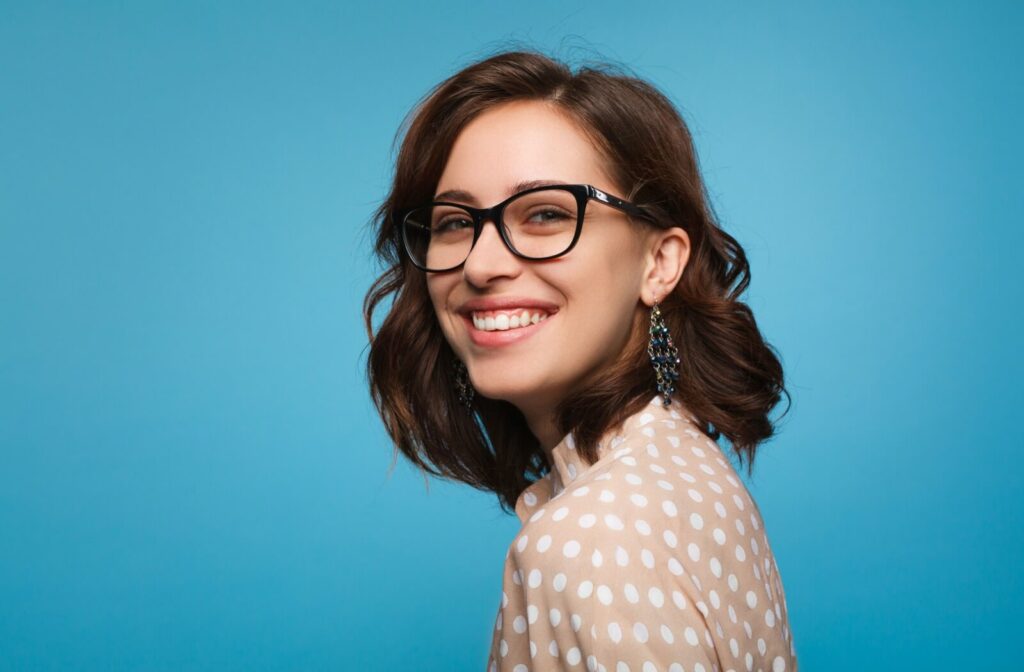 A person wearing black glasses smiling confidently against a blue background highlighting minimalist yet fashionable frames