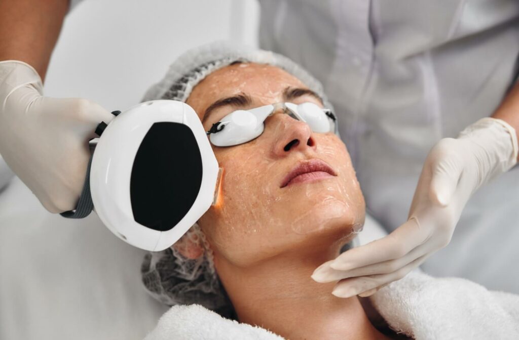 A person lying down with protective goggles receives an IPL treatment from a professional wearing gloves in a clinical setting.