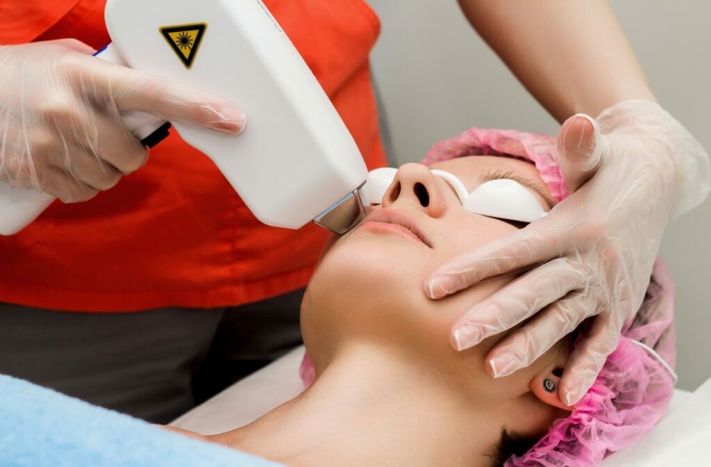 A professional wearing gloves and a red uniform performs an IPL procedure on a patient with protective eye shields