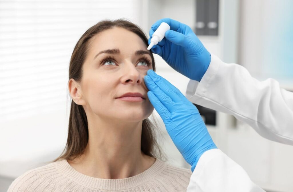 Woman receiving eye drops from an off-camera provider wearing blue gloves.