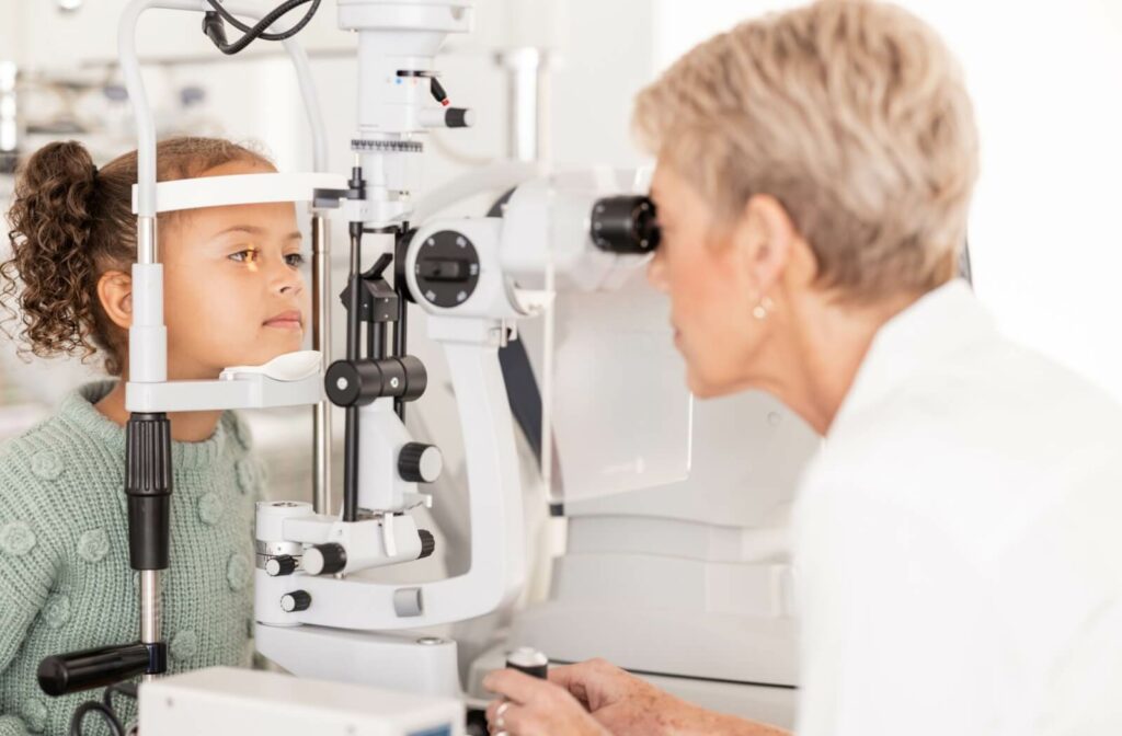 “A child sits at a slit lamp while an eye care professional examines their eyes during a comprehensive eye exam.