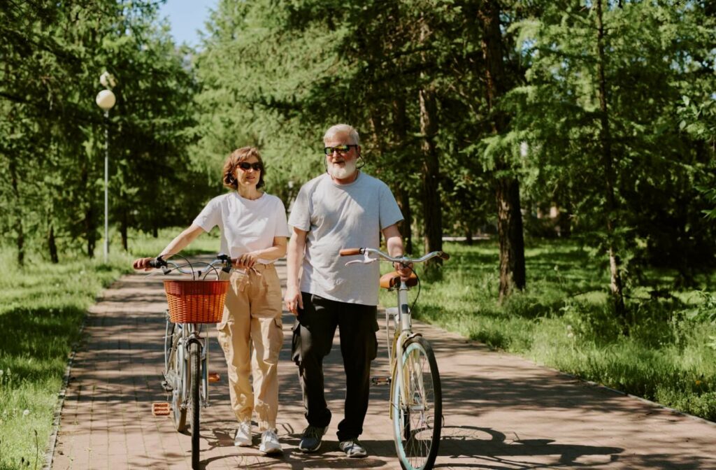 Older couple walking bikes along a park path, enjoying an active outdoor lifestyle.