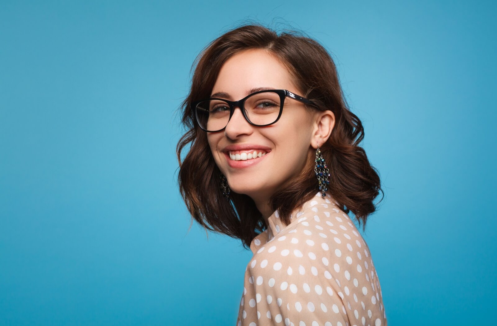 Wearing stylish black-rimmed glasses against a blue background.